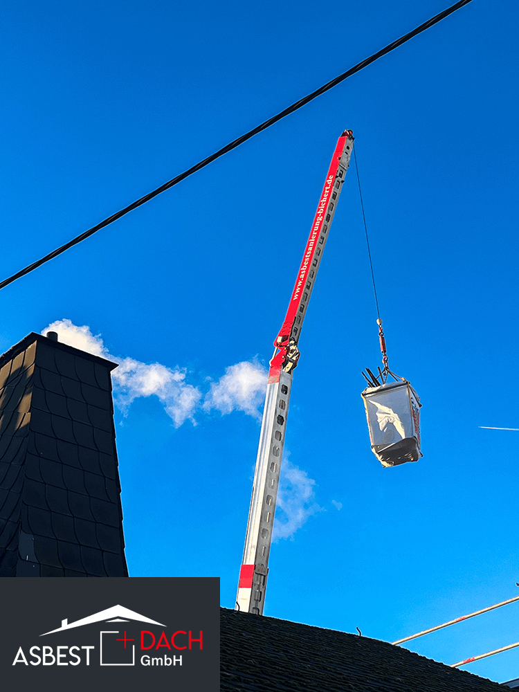 Kran hebt Big Bag mit Asbestabfällen vom Dach – Asbestsanierung durch Fachbetrieb bei klarem Himmel.