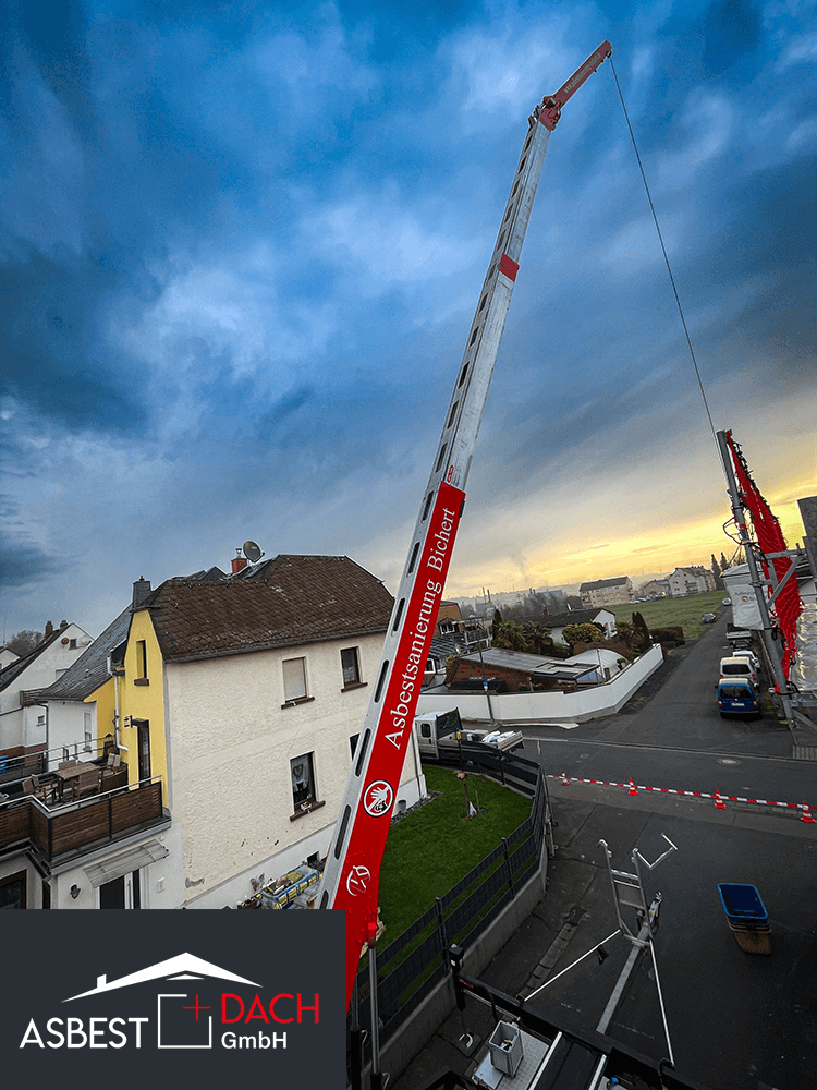 Großkran der Asbestsanierung Bichert im Einsatz bei Dachsanierung, Sonnenuntergang über Wohngebiet im Hintergrund.