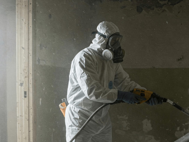 Asbestsanierung im Westerwald Fachgerechte Asbestsanierung im Westerwald: Ein Arbeiter in Schutzanzug und Atemschutzmaske entfernt asbesthaltige Materialien unter sicheren Bedingungen.